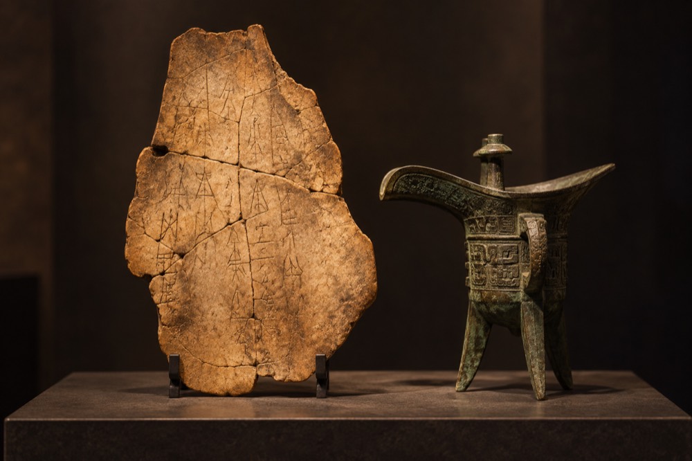 Archaeological illustration of an oracle bone and bronze ritual vessel, showing why Shang marriage and kinship are better documented than those of the Xia